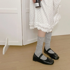 Detail of grey mesh socks with white ribbons paired with black Mary Jane shoes