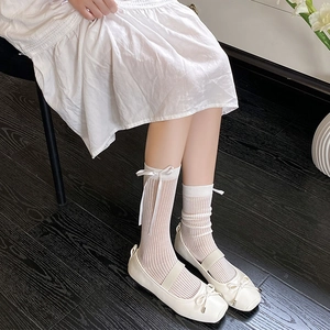 Detail of white mid-calf socks with silk bows and ribbed texture paired with Mary Janes