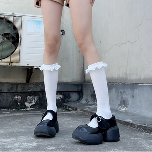 Detail of white ruffle lace trim socks paired with black patent leather platform shoes