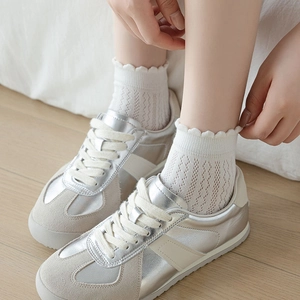 Detail of white vintage lace socks with hollow pattern worn with silver sneakers