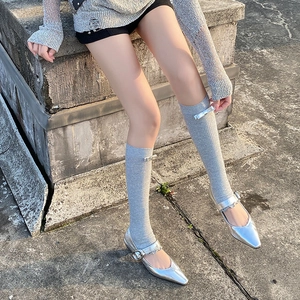 Detail of silver Mary Jane shoes with grey ribbed socks featuring a small metallic bow