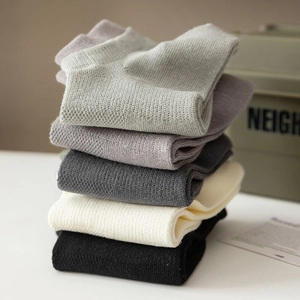 Close-up of stacked breathable mesh crew socks in neutral grey, cream, and black tones