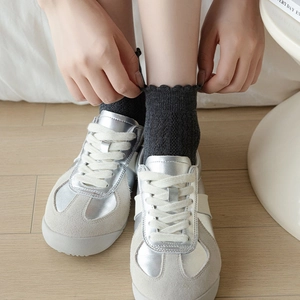 Close-up of silver metallic sneakers and grey ruffle knit socks on wooden floor
