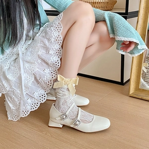Nahaufnahme weißer Spitzensocken mit gelber Samtschleife und weißen Mary-Jane-Schuhen