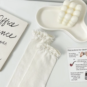 Detail of white rib-knit socks featuring delicate lace trim and pearl bead embellishments