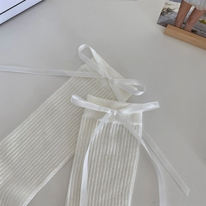 Detail of white ribbed ballet socks featuring a satin ribbon bow and knit texture