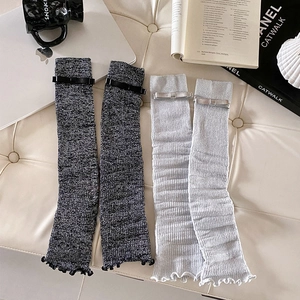 Detail of knitted leg warmers featuring elegant bow ribbons and ruffled edges in grey tones