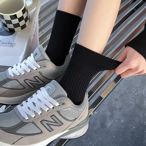 Close-up of black ribbed crew socks paired with silver retro sneakers on a metal bench