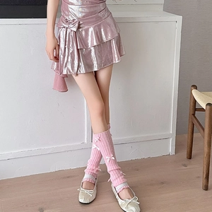 Detailed view of pink bow leg warmers styled with a metallic pleated skirt and ballet flats