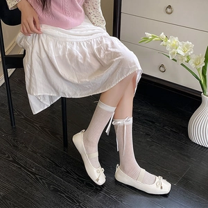 Close-up of white ballet flats with bow details and striped ribbon mid-tube socks
