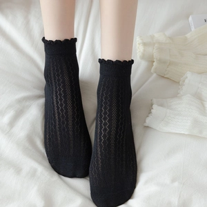 Detail of black hollow mesh socks with ruffled lace cuffs and geometric patterns
