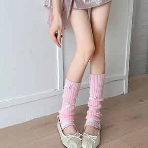 Detail of pink ribbed knit leg warmers with white bows styled with metallic flat shoes