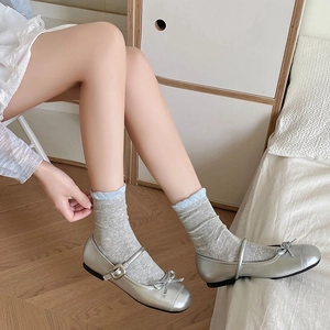 Silver Mary Jane shoes with bow detail and buckle strap on a light wood floor