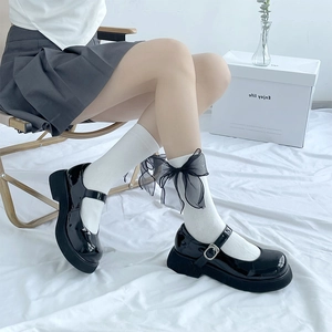 Détail de chaussettes blanches avec nœuds en tulle noir et chaussures Mary Jane compensées