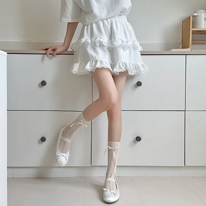 Détail de chaussettes en résille blanche avec nœuds, ballerines et jupe en dentelle