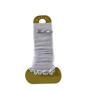 Light gray ballet style leg warmers with ribbon bows and ruffle edges on card
