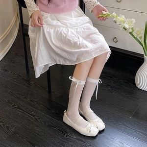 Detail of white Mary Jane shoes and vertical striped socks with ribbon bow accents