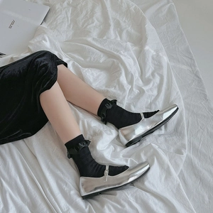 Silver Mary Jane flats with buckle strap and black ruffle socks on white bedding