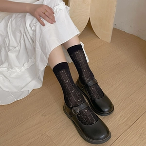 Détail de chaussettes noires à motif cœur avec chaussures Mary Jane et jupe blanche