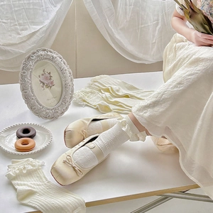 Close-up of white lace ruffle socks with cream satin ballet flats in a vintage setting