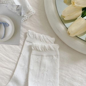 Detail of white cotton socks with bow patterns and ruffled cuffs on fabric background