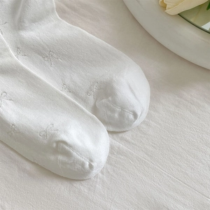 Close-up of white breathable socks featuring delicate jacquard bow patterns and texture
