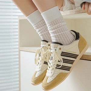 Gros plan de baskets rétro en cuir crème avec daim jaune et chaussettes blanches côtelées