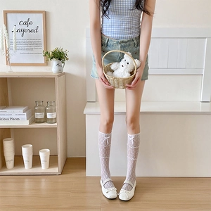 Détail de chaussettes hautes en dentelle blanche avec mesh et nœuds en satin