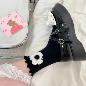 Close-up of black platform Mary Janes with a white bow and floral knit socks