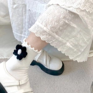 Detail of white cotton socks with 3D crochet flowers and ruffled edges paired with shoes