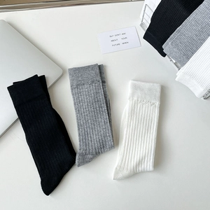 Detailed knit texture of white, black, and grey vertical ribbed calf socks on white desk