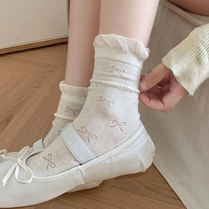 Close-up of cream white socks with brown bow patterns and ruffled edges details