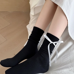 Détail de chaussettes mi-hautes noires avec nœuds en satin blanc et maille côtelée