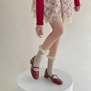Red patent leather Mary Jane shoes with cream lace bow socks on a white pedestal