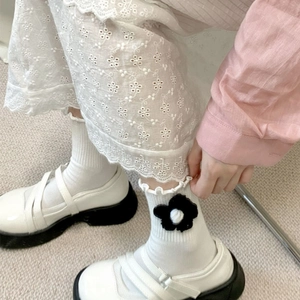 White ruffle socks with 3D floral accents and wavy cuffs worn with Mary Jane shoes