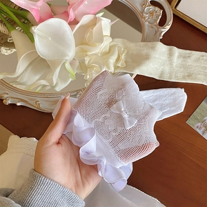 Detail of white lace mesh socks featuring delicate bow and ruffled edges in close-up shot
