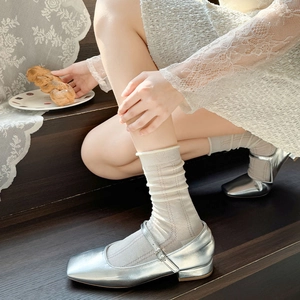 Close-up of white lace mesh socks with heart cutouts paired with silver Mary Jane shoes