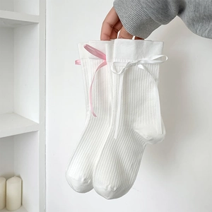 Détail de chaussettes mi-mollet en coton blanc côtelé avec nœuds roses et texture