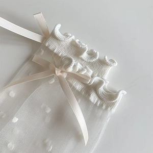 Close-up of white sheer polka dot mesh socks with ruffled cuffs and satin ribbon bows