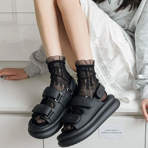 Close-up of black double-strap platform sandals worn with elegant floral lace socks