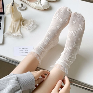 Detailed view of white floral embroidery and frilly lace trim on sheer mesh socks