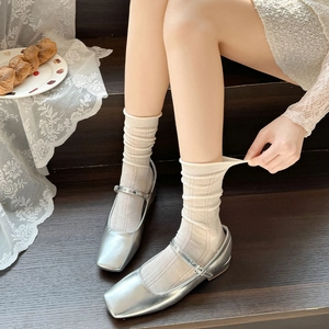 Close-up of silver Mary Jane flats with beige ribbed socks on a rustic wooden step