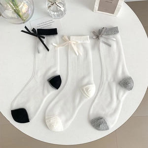 Three pairs of sheer mesh bow socks in black, beige, and grey displayed on a white table