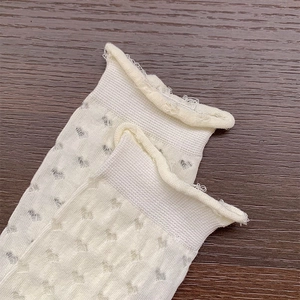 Detail of white mesh socks with heart cut-out patterns and frilly edges on wood