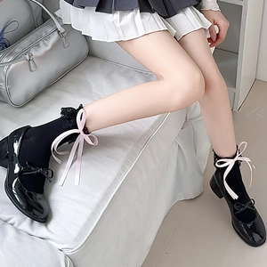Détail de chaussettes en dentelle noire avec nœuds roses et chaussures Mary Jane