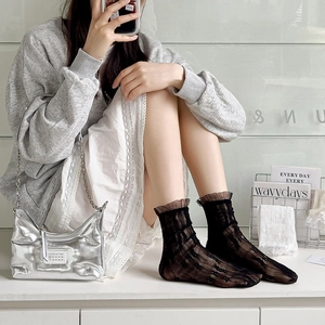 Detail of sheer black lace socks with ruffled cuffs paired with a silver handbag