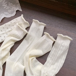 Detail view of white mesh socks with floral textures and ruffled cuffs on wood surface