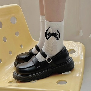 Detail of white knit socks with black bows paired with platform Mary Jane leather shoes