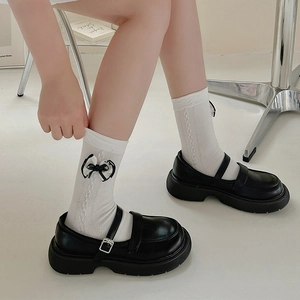 Detailed view of white knit socks with black bows paired with black Mary Jane shoes