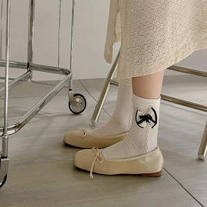 Close-up of beige round-toe ballet flats with white jacquard socks and bow details